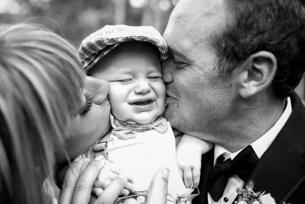 Bride and groom kissing baby on cheeks black and white
