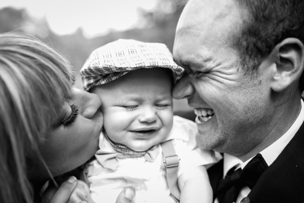 Bride and groom kissing baby on cheeks black and white