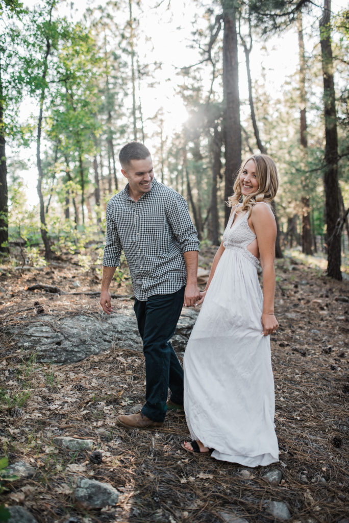 Emily and Andrew walking through forest at Arizona engagement 