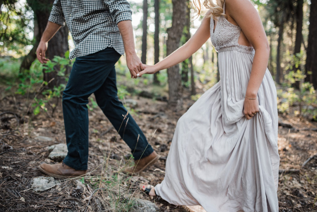 Emily and Andrew walking through forest at Arizona engagement 