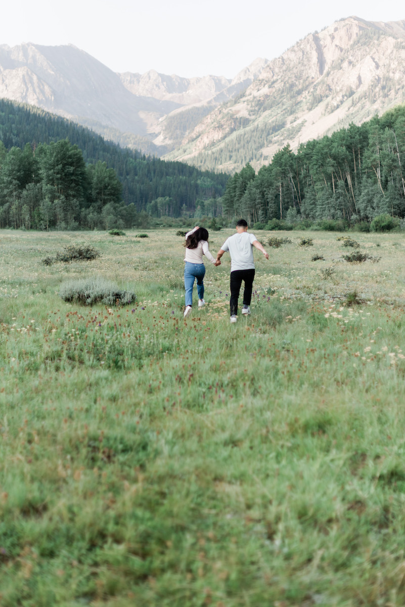 Couple running in field at Aspen engagement 