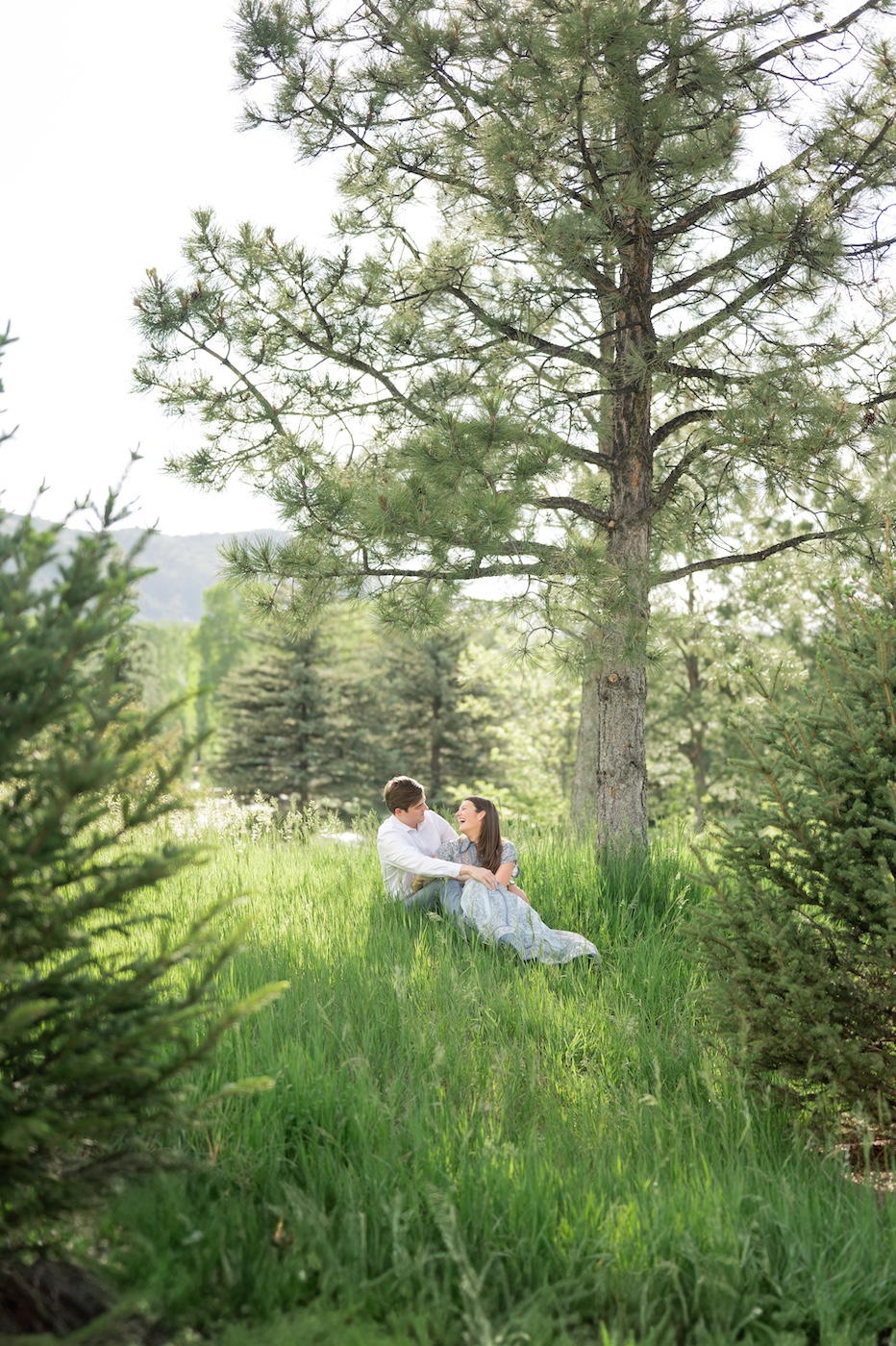 Far away image of couple sitting in field together and laughing.
